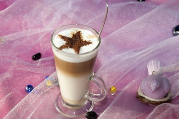 Very tasty cappuccino in a high glass cup with a chocolate star top on a table with pink stuff. Top view
