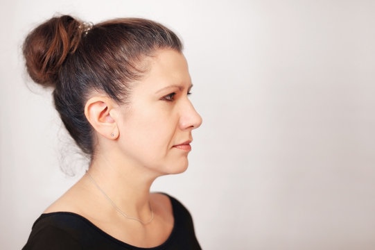 Portrait Of A Sad Woman In A Profile On A Gray Background. She Looks To The Side And Gets Sad Because Her Hair Is Gray