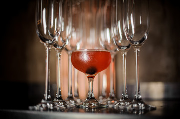 Elegant tasty red alcoholic cocktail among empty champagne glasses