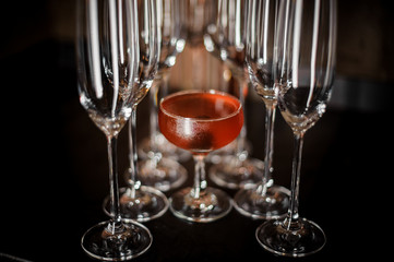 Glass filled with tasty red alcoholic drink with empty champagne glasses