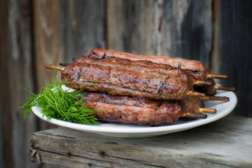 Lulya kebab from meat on a white plate and wooden board with dill.