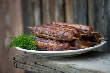 Lulya kebab from meat on a white plate and wooden board with dill.