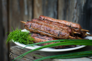 Lulya kebab from meat on a white plate and wooden board with dill and green onions.