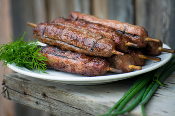 Lulya kebab from meat on a white plate and wooden board with dill and green onions.
