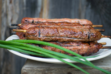 Lulya kebab from meat on a white plate and wooden board with green onions.