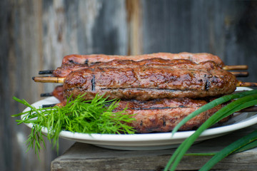 Lulya kebab from meat on a white plate and wooden board with dill and green onions.