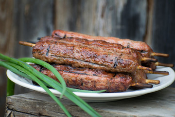 Lulya kebab from meat on a white plate and wooden board with green onions.
