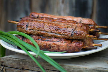Lulya kebab from meat on a white plate and wooden board with green onions.