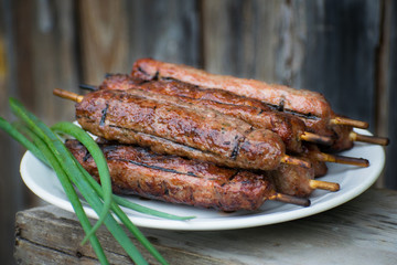 Lulya kebab from meat on a white plate and wooden board with green onions.