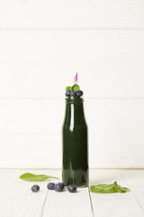 selective focus of bottle of spirulina smoothie with mint leaves, blueberries and drinking straw on wooden table