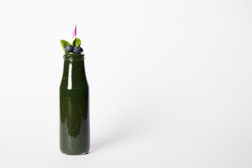 bottle of spirulina smoothie with mint leaves, blueberries and drinking straw on white background