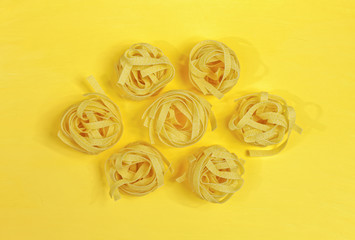 Close up of a raw dry italian pasta fettuccine on bright yellow background. Shooting with bold color.
