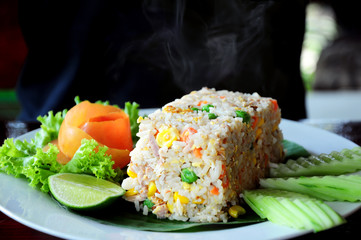 Fried rice is hot and there is smoke out served with vegetable and lemon.