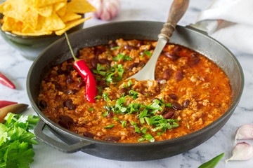 Mexican and American food Chili con carne served with nachos, pepper and herbs.