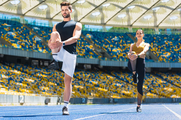 young sportive couple warming up legs before jogging on running track at sports stadium