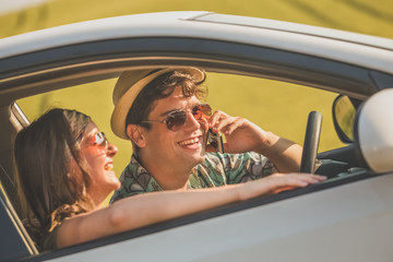 Fashionable couple sitting in car interior and using mobile phone.