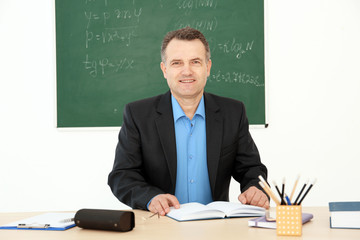 Male teacher working at table in classroom