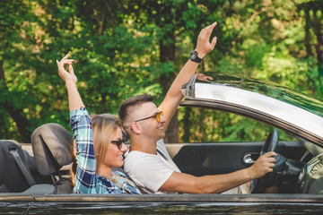 Young couple enjoying road trip with hands up inside of their convertible car.