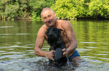 Owner plays with his schnauzer dog on the river bank