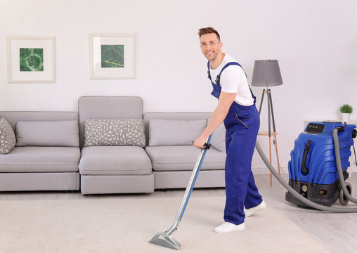 Male Worker Removing Dirt From Carpet With Professional Vacuum Cleaner Indoors