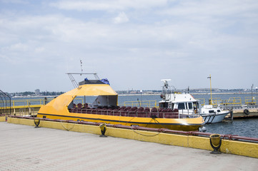 The boat for walking is moored to the pier, at the passenger terminal of the port. The bright yellow boat black stripe looks impressive, against the backdrop of the sea pier. 