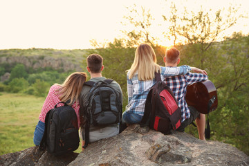 Group of young people with backpacks and guitar in wilderness. Camping season