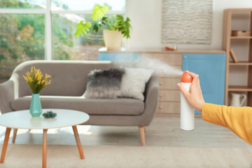 Woman spraying air freshener at home