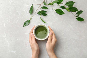 Woman with cup of matcha tea and leaves at table, top view
