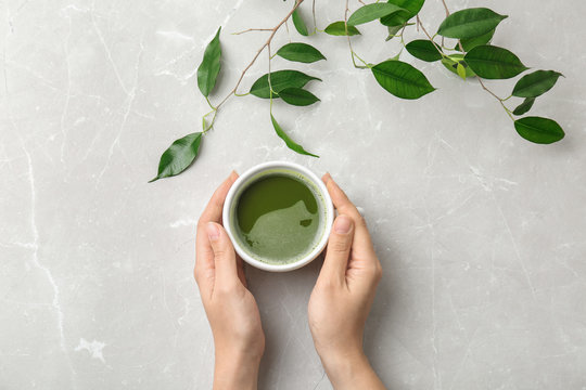 Woman With Cup Of Matcha Tea And Leaves At Table, Top View