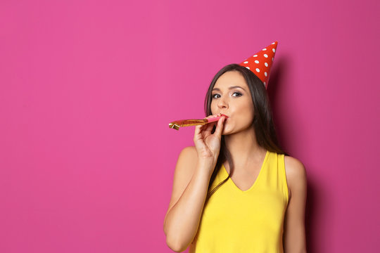 Young woman with party blower on color background. Birthday celebration