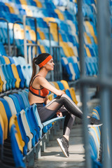 Naklejka na ściany i meble side view of attractive young woman sitting on tribunes at sports stadium