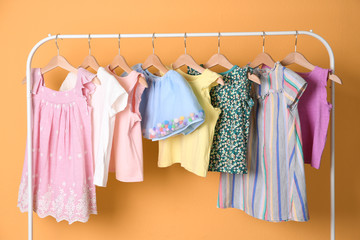Rack with stylish child clothes on color background