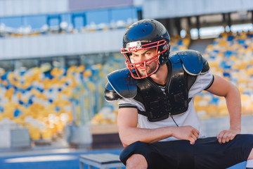 serious young american football player sitting at sports stadium