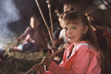 Little girl with marshmallow near bonfire at night. Summer camp