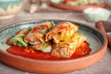 Plate with stuffed cabbage leaves in tomato sauce on table