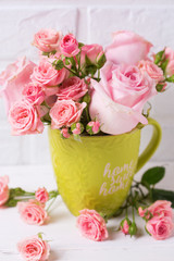 Pink roses flowers in green cup against  white brick wall.