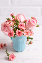 Pink roses flowers in blue cup against  white brick wall. Floral still life.