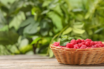 Wicker basket with ripe aromatic raspberries on table against blurred background