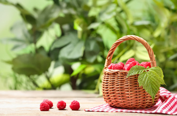 Fototapeta na wymiar Wicker basket with ripe aromatic raspberries on table against blurred background