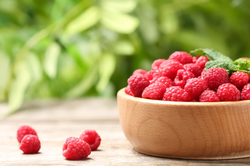 Bowl with ripe aromatic raspberries on table against blurred background