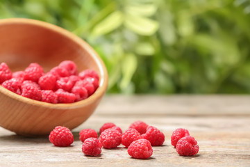Bowl with ripe aromatic raspberries on table against blurred background