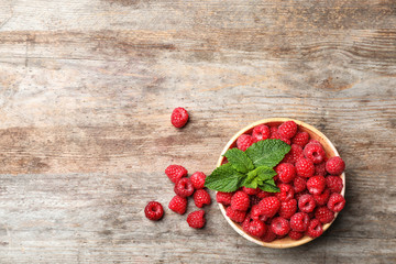 Bowl with ripe aromatic raspberries on wooden table, top view