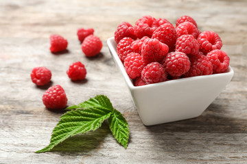 Bowl with ripe aromatic raspberries on wooden table