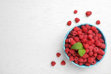 Bowl with ripe aromatic raspberries on wooden table, top view