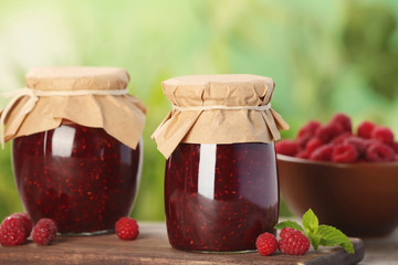 Jars with delicious raspberry jam on table against blurred background