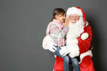 Little girl whispering in authentic Santa Claus' ear on grey background