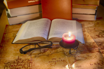Vintage still life: a book, glasses and a burning candle against the background of stacks of books and an ancient world map