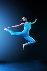 Beautiful young and fit ballet dancer jumping on a black background. Dance and sport concept.