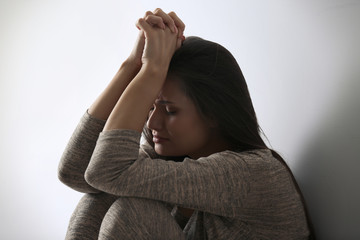 Depressed young woman sitting near light wall