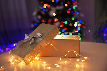 Gift box with fairy lights and blurred Christmas tree on background
